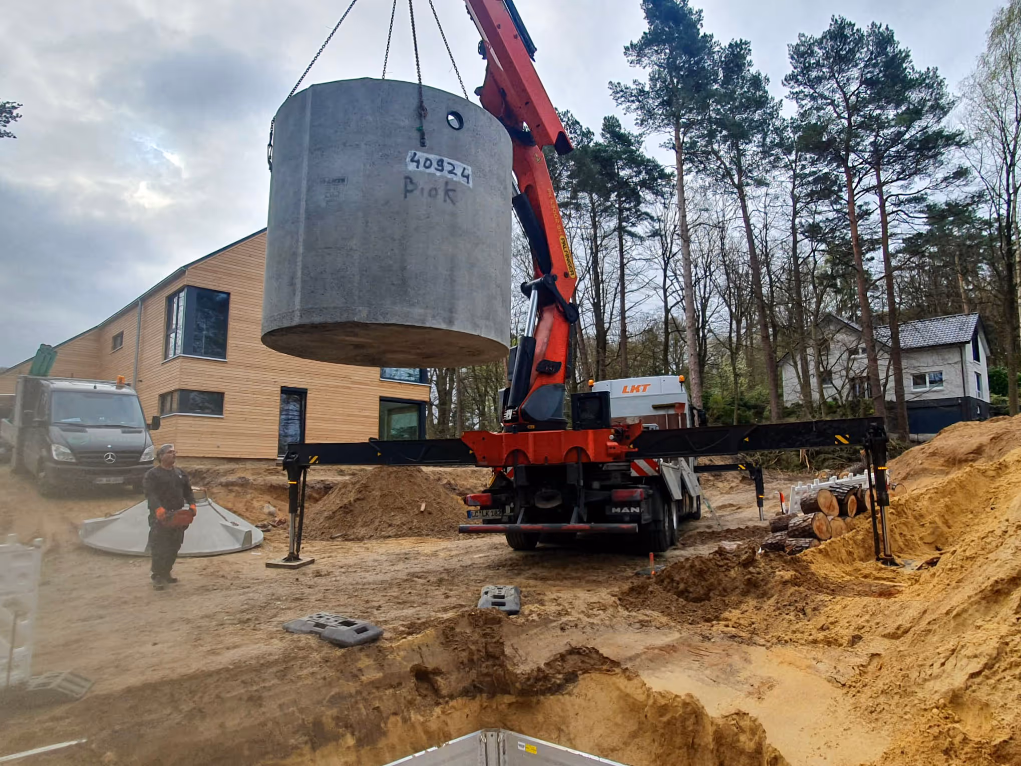 Ladekran hebt Betonbehälter einer Kleinkläranlage in die Baugrube