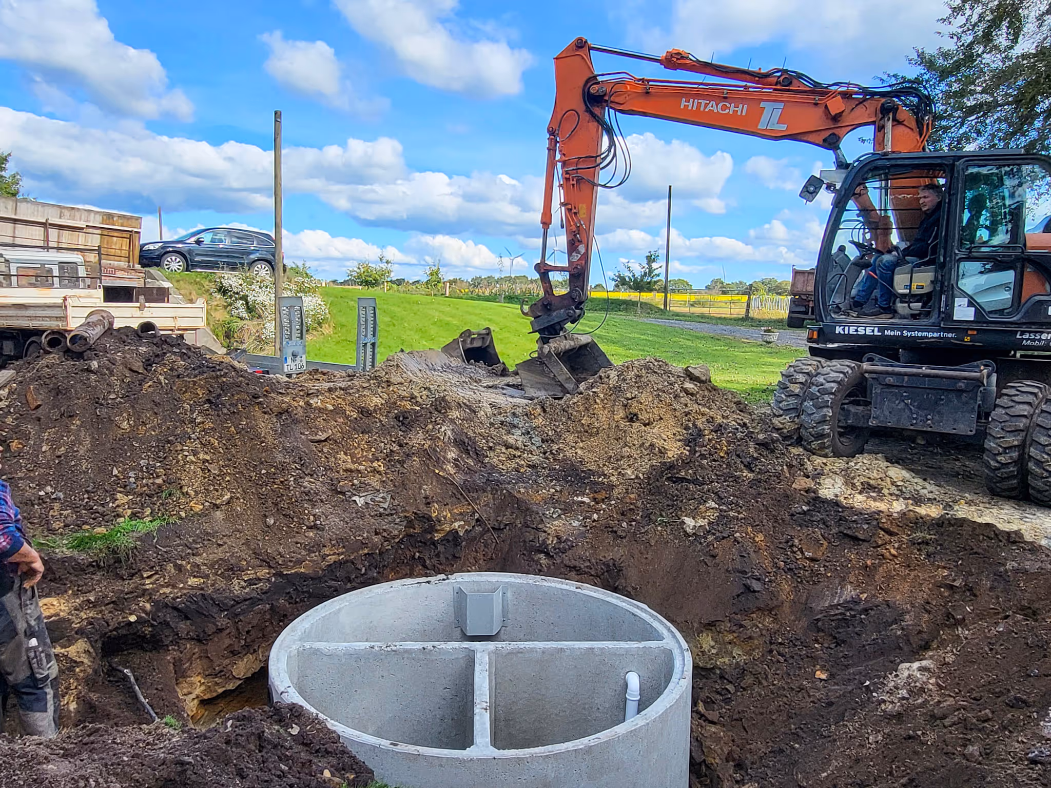 Mehrkammergrube aus Beton in der Baugrube, Bagger im Hintergrund